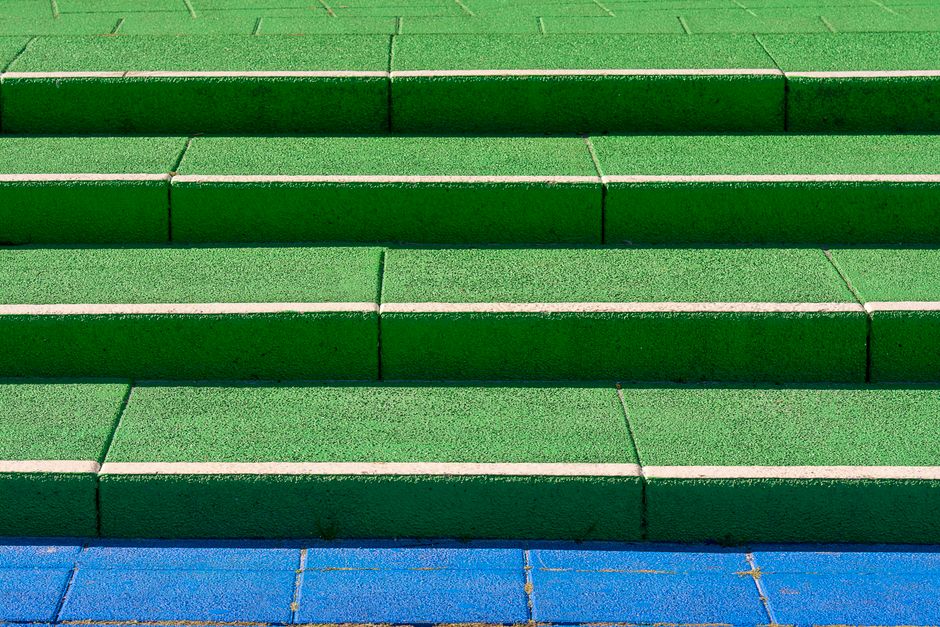 Close-up view of outdoor stairway with six steps constructed from green terrazzo tiles with white grout lines, leading up to a landing. The surface of each step appears clean and well-maintained, with a smooth and polished finish that reflects natural light. The steps are evenly aligned, with no visible debris, dust, or stains, suggesting recent surface cleaning or regular maintenance. The lighting is natural, enhancing the vibrant color and texture of the tiles. The blue tiled landing at the bottom contrasts with the green steps, indicating a multi-level residential or commercial entrance area where surface cleaning and upkeep are a focus, consistent with Holland Park Cleaner's emphasis on hygiene and maintenance solutions for flats and staircases.