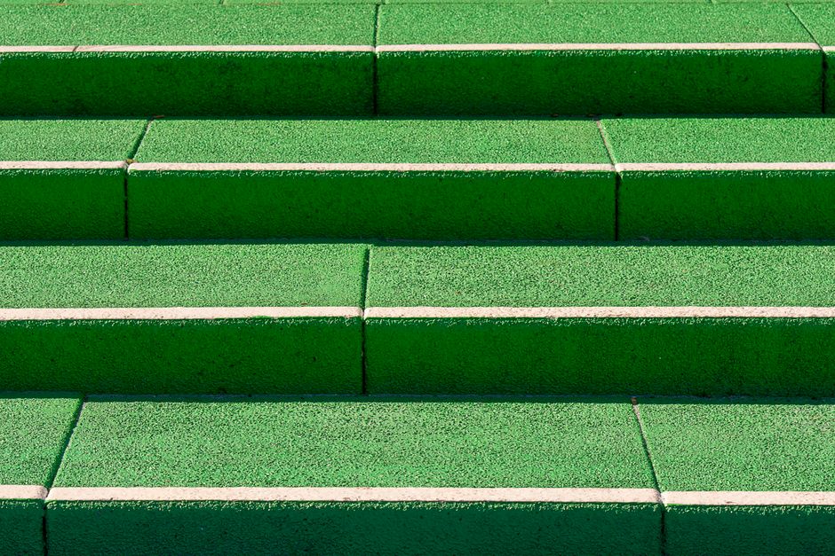 Close-up view of outdoor stairway with six steps constructed from green terrazzo tiles with white grout lines, leading up to a landing. The surface of each step appears clean and well-maintained, with a smooth and polished finish that reflects natural light. The steps are evenly aligned, with no visible debris, dust, or stains, suggesting recent surface cleaning or regular maintenance. The lighting is natural, enhancing the vibrant color and texture of the tiles. The blue tiled landing at the bottom contrasts with the green steps, indicating a multi-level residential or commercial entrance area where surface cleaning and upkeep are a focus, consistent with Holland Park Cleaner's emphasis on hygiene and maintenance solutions for flats and staircases.